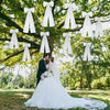 Un(e) marié(e) et mariée s'embrassent sous une canopée de nœuds de satin blancs suspendus sur des branches d'arbre vertes en 