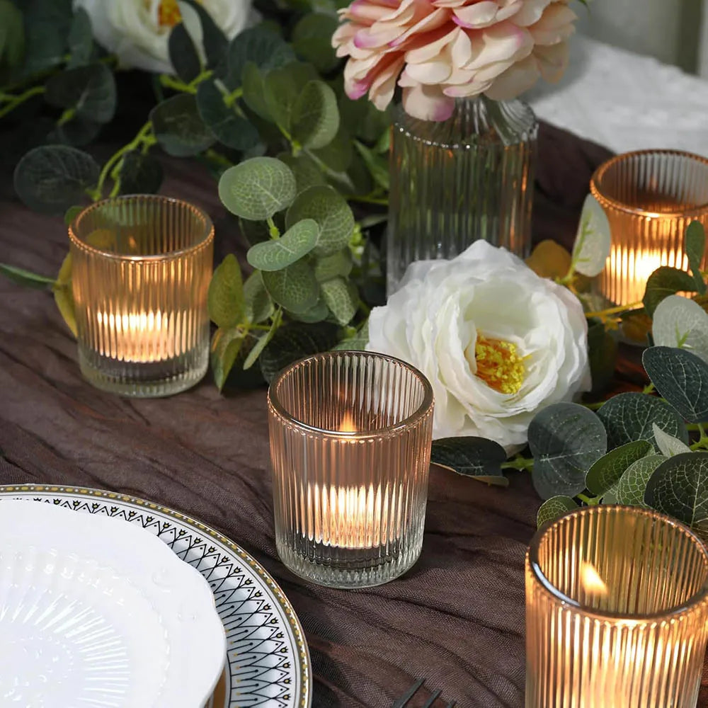 A collection of vintage stripe glass votive candle holders and white roses arranged on a wooden surface.