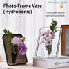 A clear acrylic photo frame vase holding purple flowers and greenery.