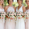 Four brides in light pink and white gowns holding silk rose bridal bouquets