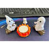 A set of three white ghost figurines, one of which is a campfire, displayed on a dark surface.