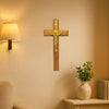 A wooden crucifix with a gold Jesus figure mounted on a beige wall above a light fixture.