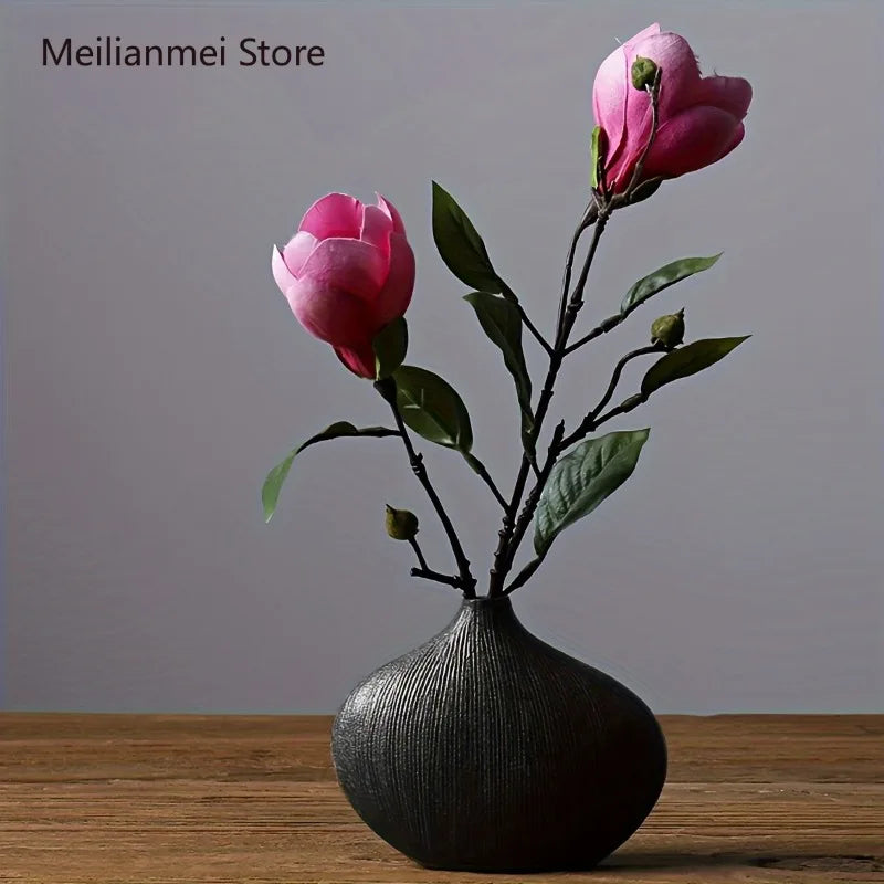 A pink rose branch in a dark vase on a wooden surface.
