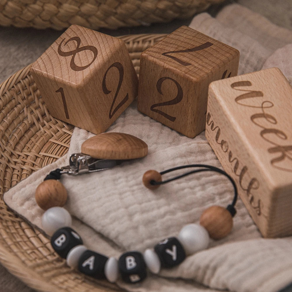 A collection of wooden baby milestone cards and a wooden bracelet are displayed on a woven tray and linen fabric.