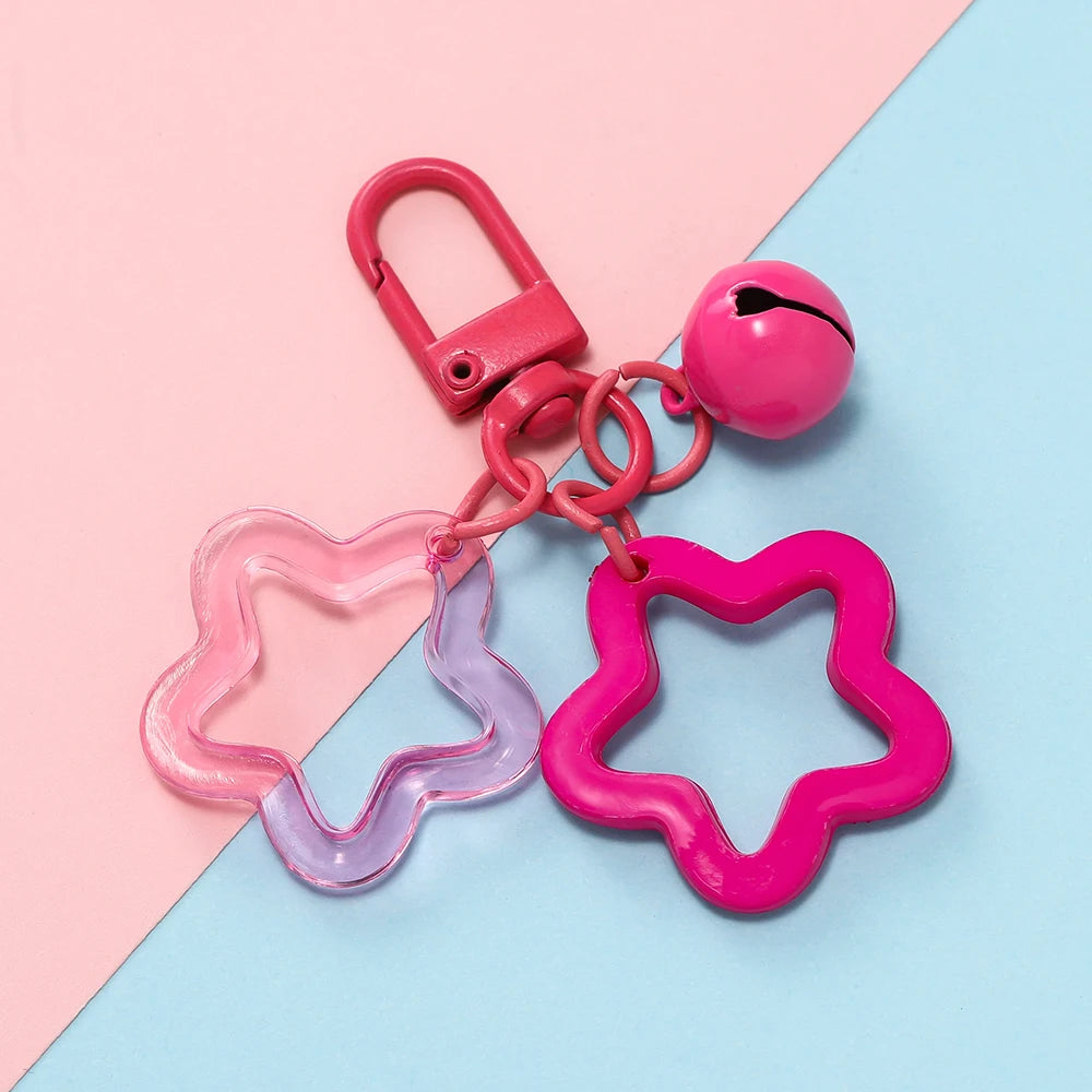 A pink and purple star charm pendant keychain with a pink clasp and chain resting on a light blue background.