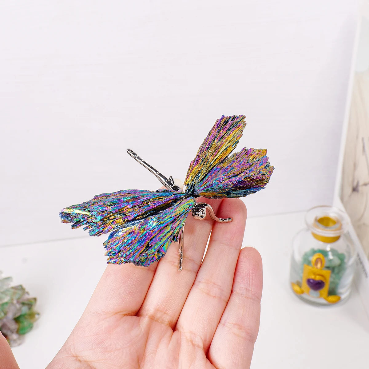 A hand holds a natural crystal tourmaline dragonfly figurine with iridescent purple and green wings.