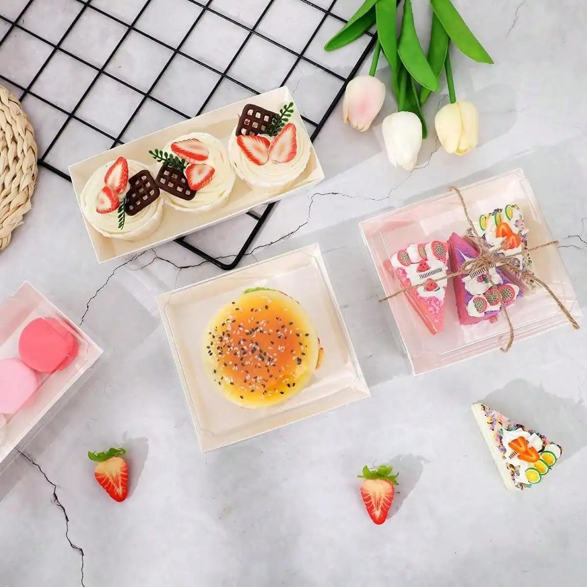 A flat lay of various pastries and fruit arranged in minimalist kraft sandwich boxes on a white marble surface.