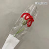 A handmade crochet tulip bouquet featuring red flowers and green stems displayed in clear plastic packaging.