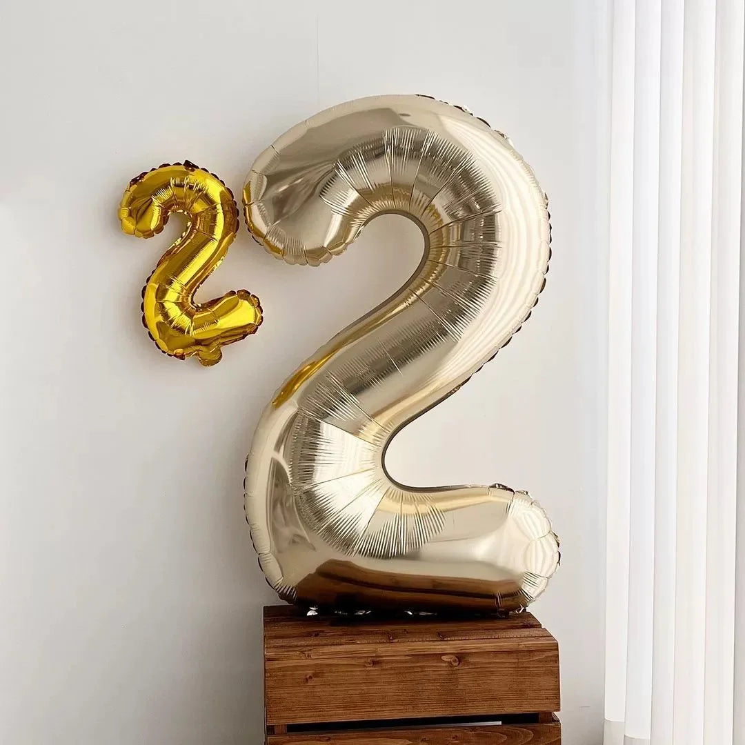 A large, gold foil number balloon shaped like the number 2, displayed on a wooden surface.