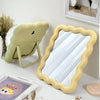 A light green wavy frame makeup mirror with a stand is displayed on a white surface.