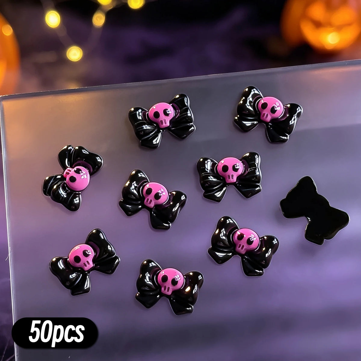 A variety pack of 50 black and pink skull resin nail charms displayed on a clear surface.