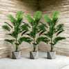 Three artificial palm trees with green monstera leaves in gray pots displayed against a textured wall.