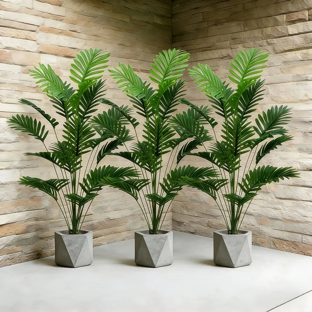 Three artificial palm trees with green monstera leaves in gray pots displayed against a textured wall.