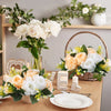 A floral arrangement featuring white and peach roses in a rustic setting with greenery and natural wood elements.