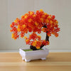 An artificial bonsai tree decoration with vibrant orange and yellow foliage planted in a white rectangular pot.