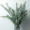 A bouquet of artificial eucalyptus stems with realistic green leaves displayed in a metallic vase.