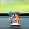 A figurine of a girl and a boy holding hands with a yellow balloon on a wooden plank for car dashboard decor.