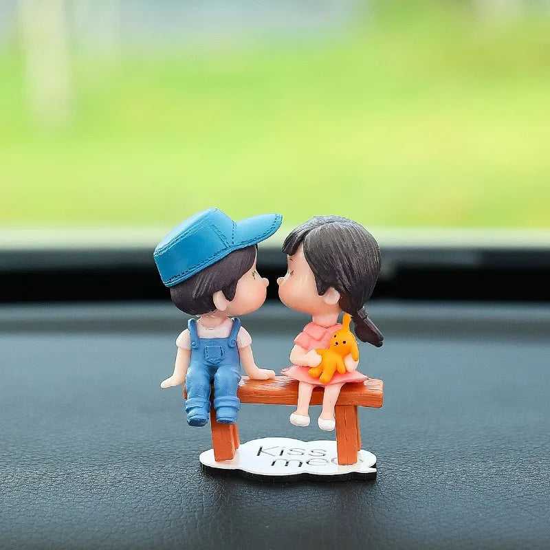 A figurine of a girl and a boy holding hands with a yellow balloon on a wooden plank for car dashboard decor.