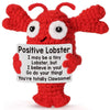 A handmade red crochet lobster doll with large eyes and an inspirational card attached.