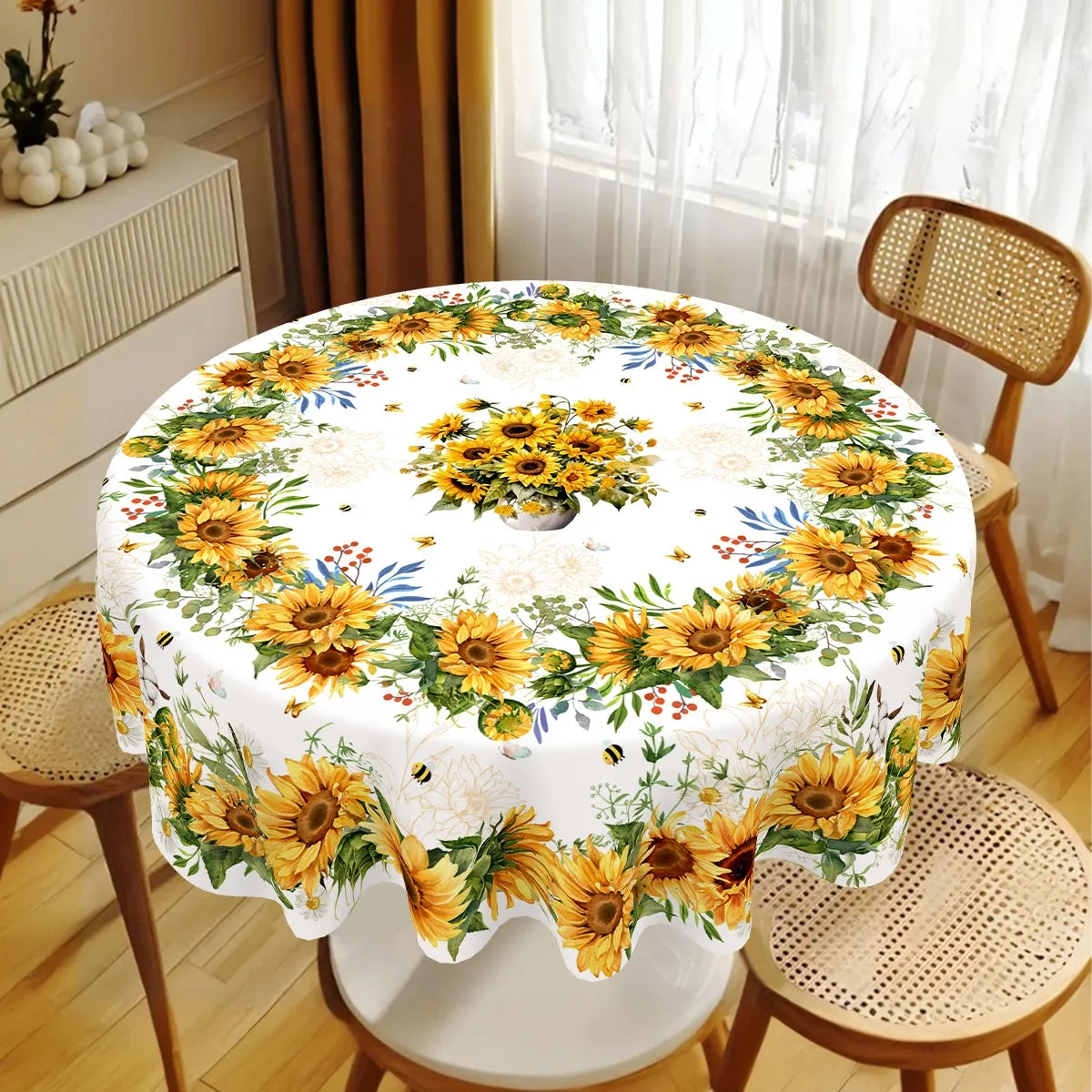 A white tablecloth with a yellow and green sunflower print is displayed on a round table in a bright room.