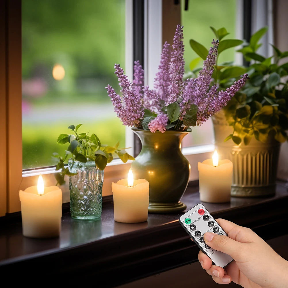 A hand holds a remote control for a set of flameless LED tea lights placed on a windowsill with flowers in the background.
