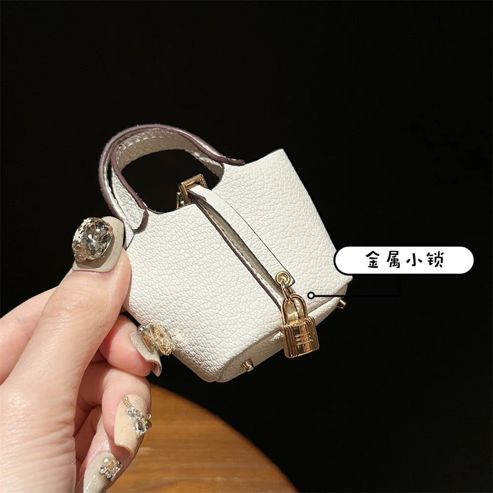 A hand holds a small, cream-colored leather handbag with a gold clasp and wrist strap against a dark background.
