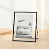 A modern black picture frame displaying a photograph of a bed with white bedding and a feather.