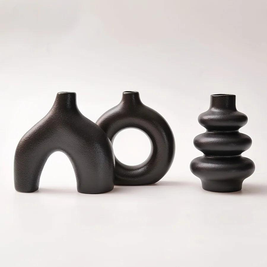 A set of three matte black ceramic vases with organic, sculptural shapes.