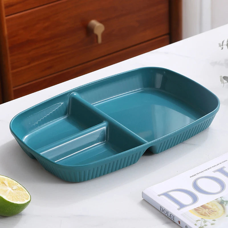 A teal 3-compartment portion control plate is displayed on a white surface next to a book.