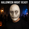 A person wearing a white sculpted ghost face mask with dark, menacing features against a dimly lit background.