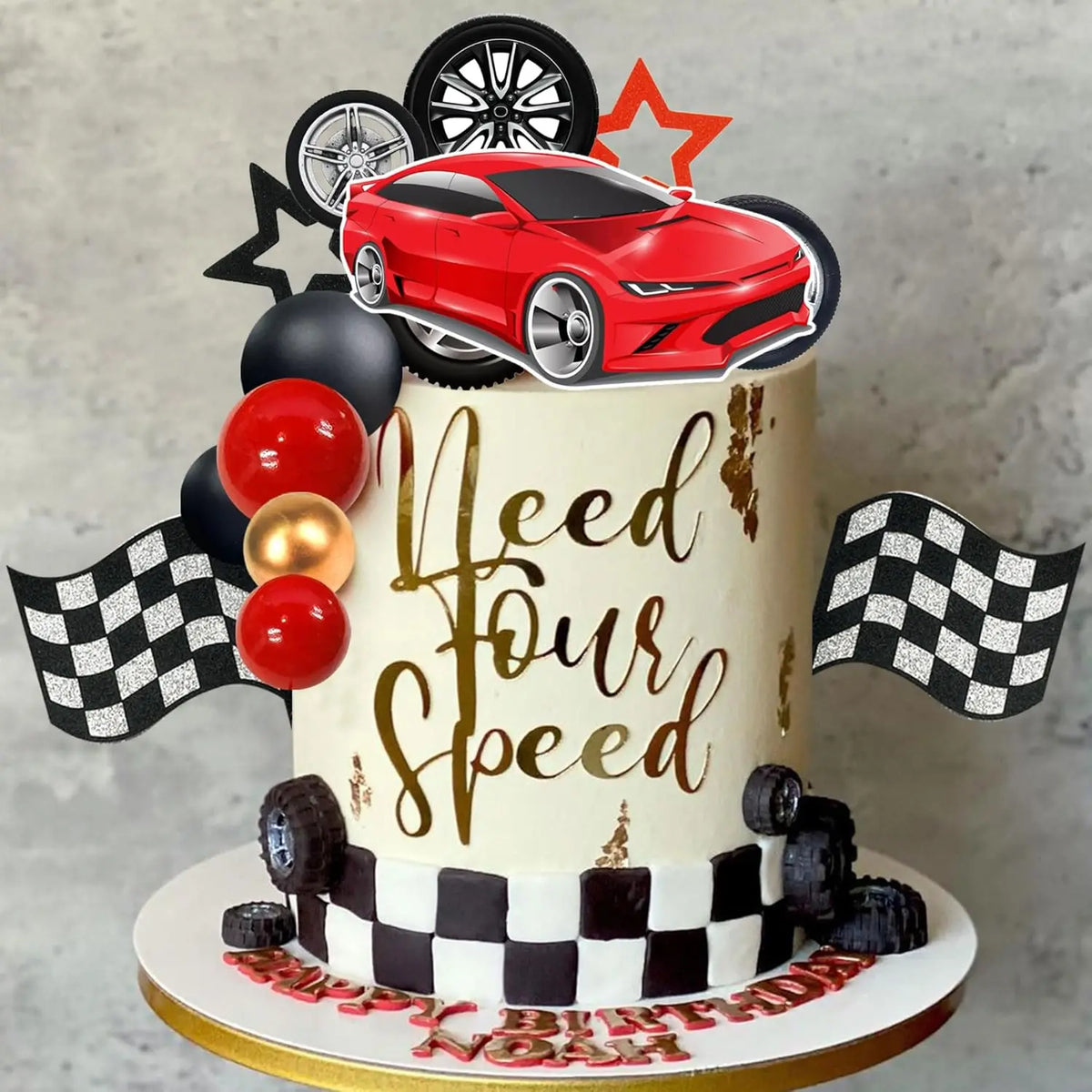 A tiered cake decorated with a red racing car topper, black and gold accents, and checkered flags.
