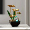 A golden lotus water fountain with green leaves and blue LED lights in a black pot.