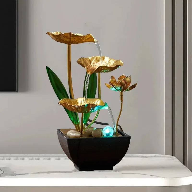A golden lotus water fountain with green leaves and blue LED lights in a black pot.