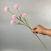 Una mano sostiene un tallo de flores artificiales de margarita de crisantemo rosa contra un fondo gris claro.