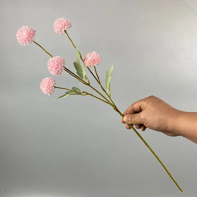 Una mano sostiene un tallo de flores artificiales de margarita de crisantemo rosa contra un fondo gris claro.
