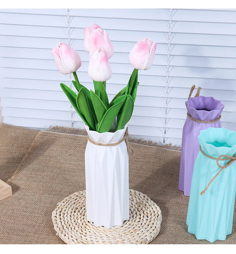 A white plastic vase with a basket design holds pink tulips against a light blue wooden background.