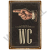 A vintage metal sign featuring a hand pointing and the letters WC on a dark background.