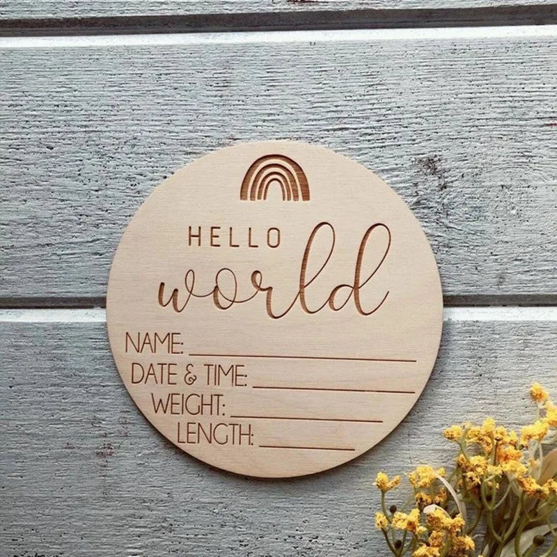 A round wooden sign with the words Hello World and lines for name, date & time, weight, and length, featuring a rainbow desig