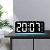 A black digital alarm clock displaying 20:07 with blue light, resting on a dark wooden surface.
