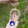 A hand holds a gold horseshoe amulet featuring an elephant charm and a large blue eye pendant.