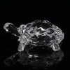 Clear glass miniature tortoise statue reflecting on a dark surface.