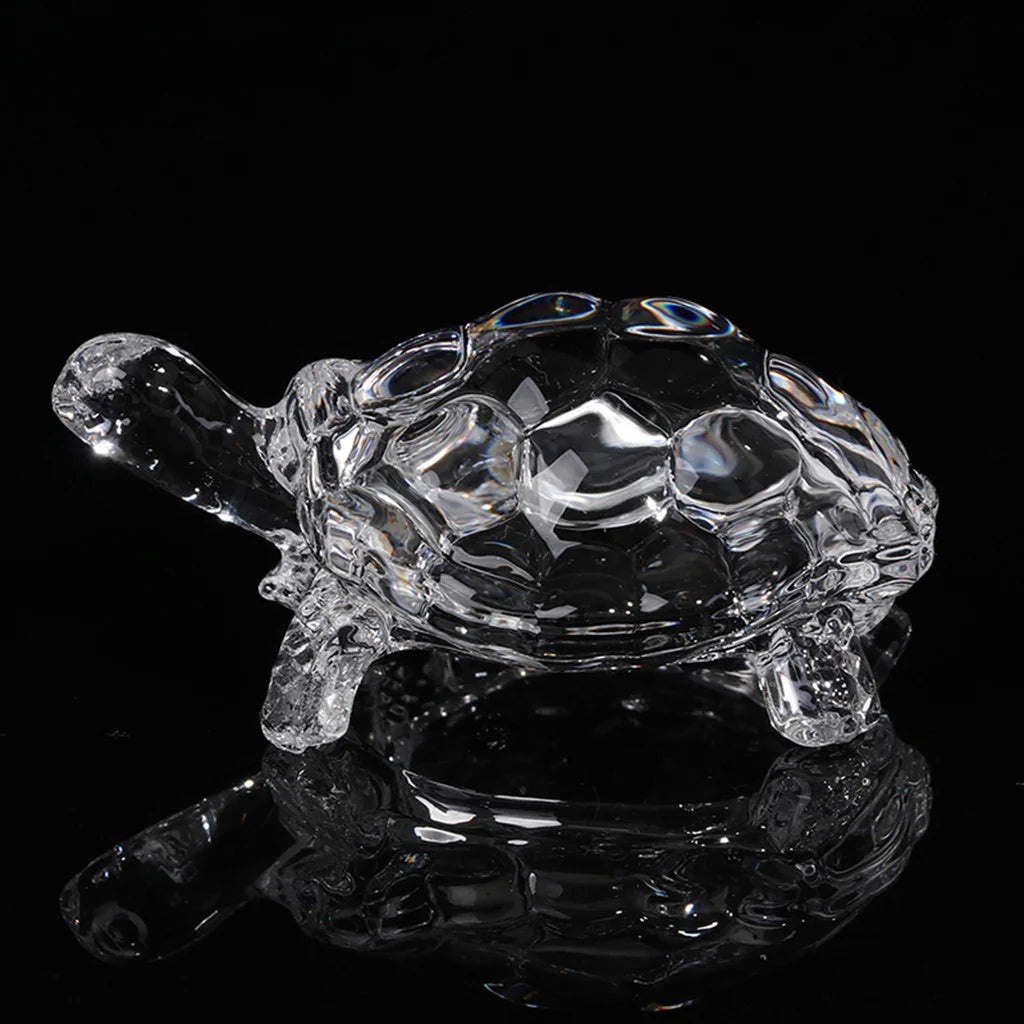 Clear glass miniature tortoise statue reflecting on a dark surface.