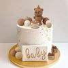 A white cake decorated with a teddy bear topper and small spherical edible decorations for a baby shower.