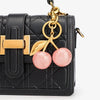Black quilted shoulder bag with gold hardware and a pink cherry resin pendant keychain