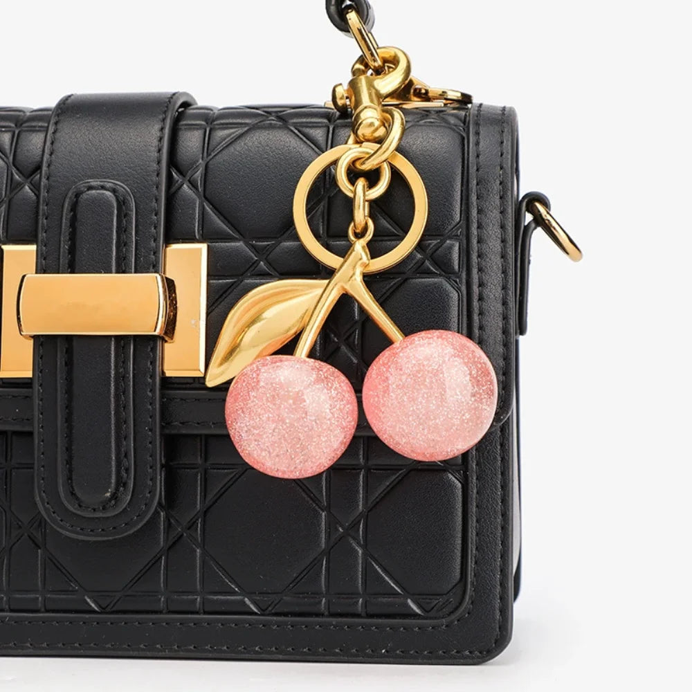 Black quilted shoulder bag with gold hardware and a pink cherry resin pendant keychain
