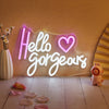 An LED neon sign spelling out Hello Gorgeous on a wall with small pink petals scattered on the floor.