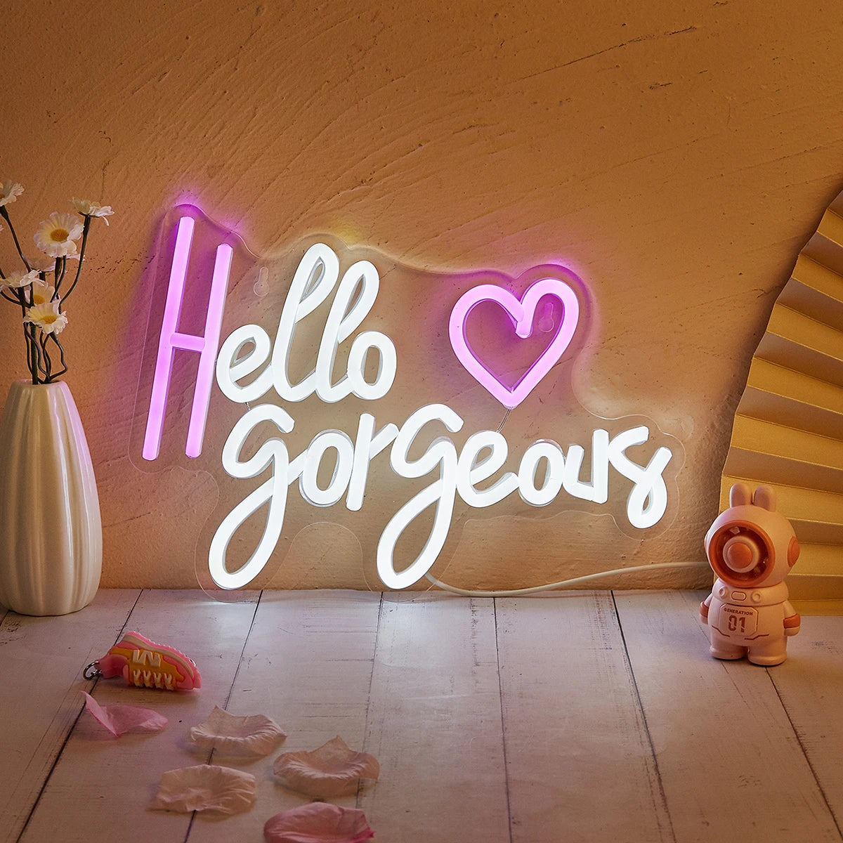 An LED neon sign spelling out Hello Gorgeous on a wall with small pink petals scattered on the floor.