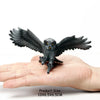A dark gray realistic figurine set of an owl, vulture, and bald eagle resting on a human hand.