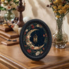 A round black framed piece of Gothic Victorian wall art featuring a detailed moon and floral design.