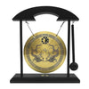 A black desktop stand holding a round brass gong with intricate carvings and a wooden mallet.